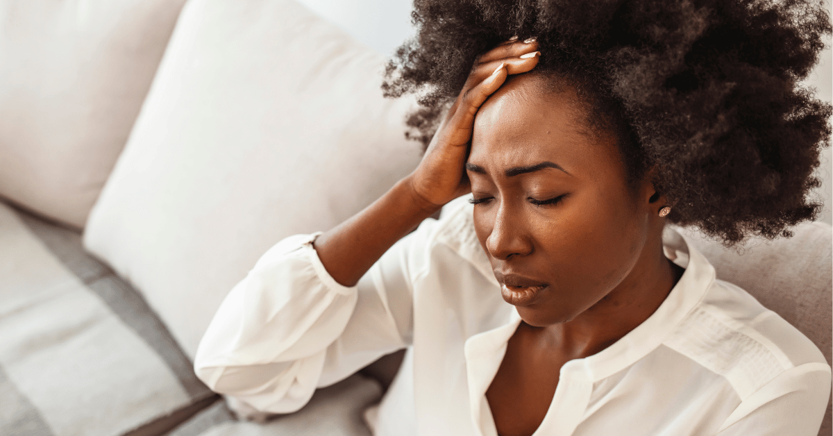 Woman experiencing stress and physical tension, holding forehead — representing the body's response to unresolved emotional weight, mind-body health blog