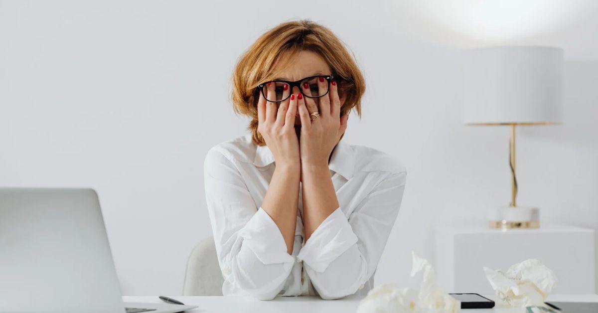 Overwhelmed woman at her desk covering her face, showing emotional stress, burnout, and money anxiety that can be released through epigenetic healing and inherited emotion clearing