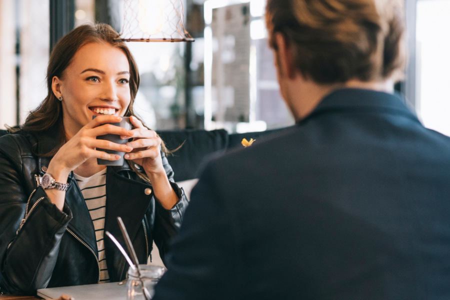 Woman smiling at date across café table, illustrating repeating relationship patterns and attraction to the same type of person