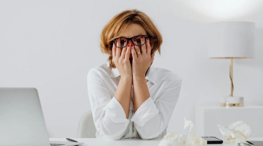 Overwhelmed woman at her desk covering her face, showing emotional stress, burnout, and money anxiety that can be released through epigenetic healing and inherited emotion clearing