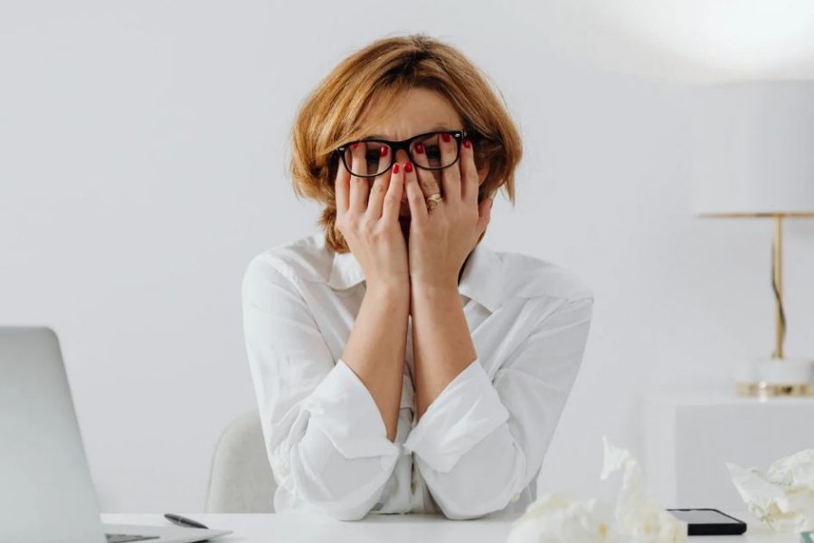 Overwhelmed woman at her desk covering her face, showing emotional stress, burnout, and money anxiety that can be released through epigenetic healing and inherited emotion clearing