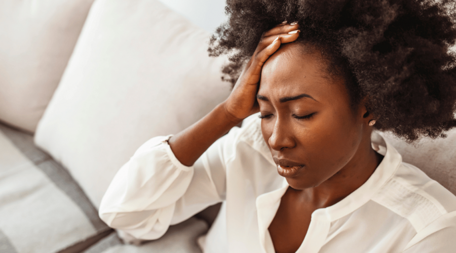 Woman experiencing stress and physical tension, holding forehead — representing the body's response to unresolved emotional weight, mind-body health blog