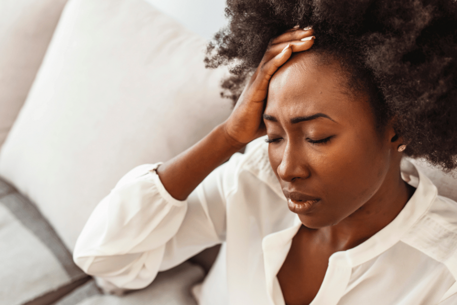 Woman experiencing stress and physical tension, holding forehead — representing the body's response to unresolved emotional weight, mind-body health blog